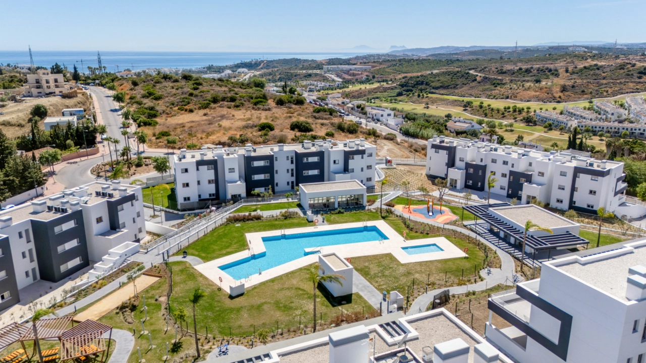 Et vidunderligt perspektiv af den færdige bebyggelse, der viser swimmingpoolene og grønne områder med havet i horisonten.