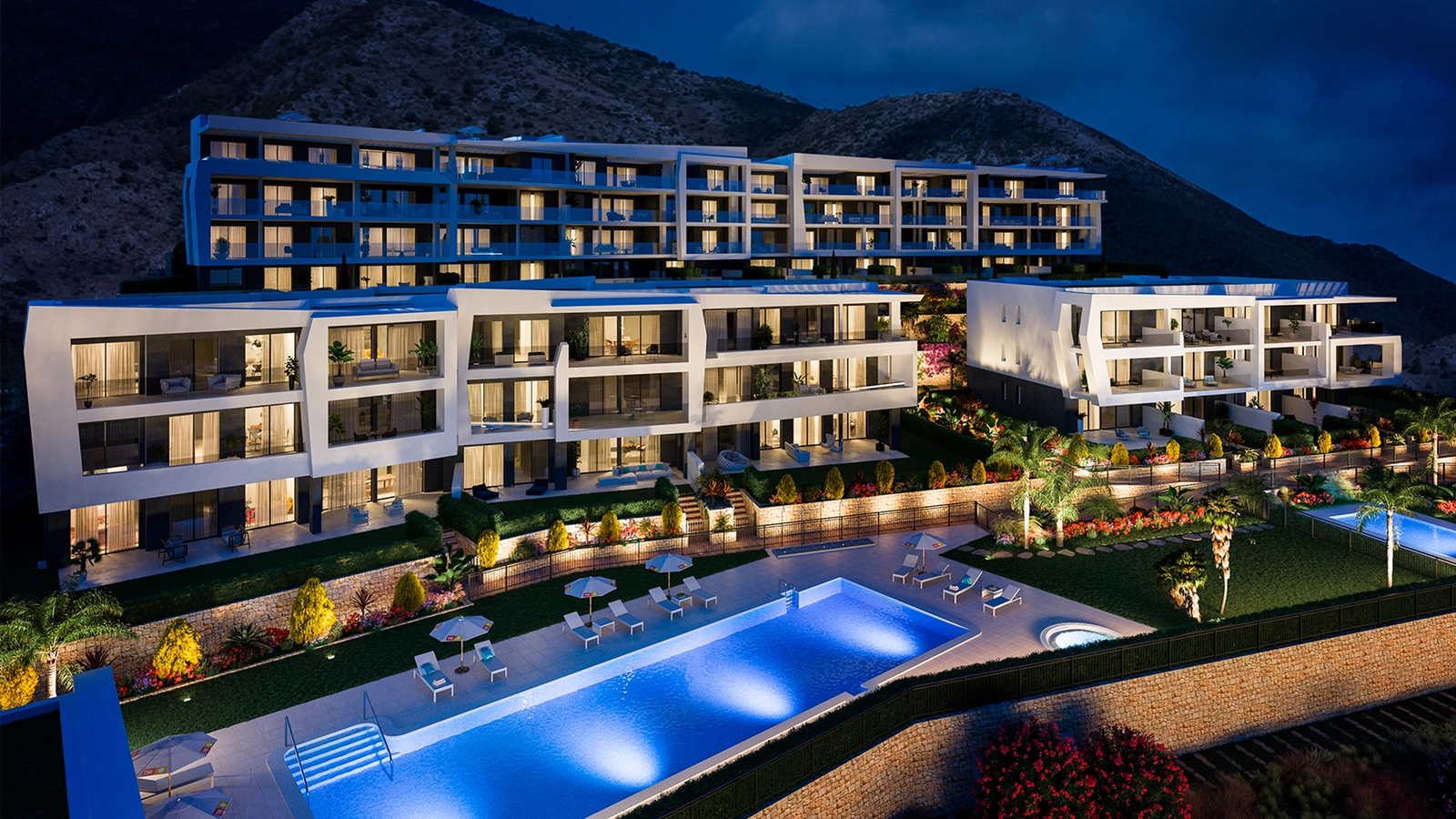 The stunning communal pool and gardens beautifully illuminated at night, creating a magical atmosphere.