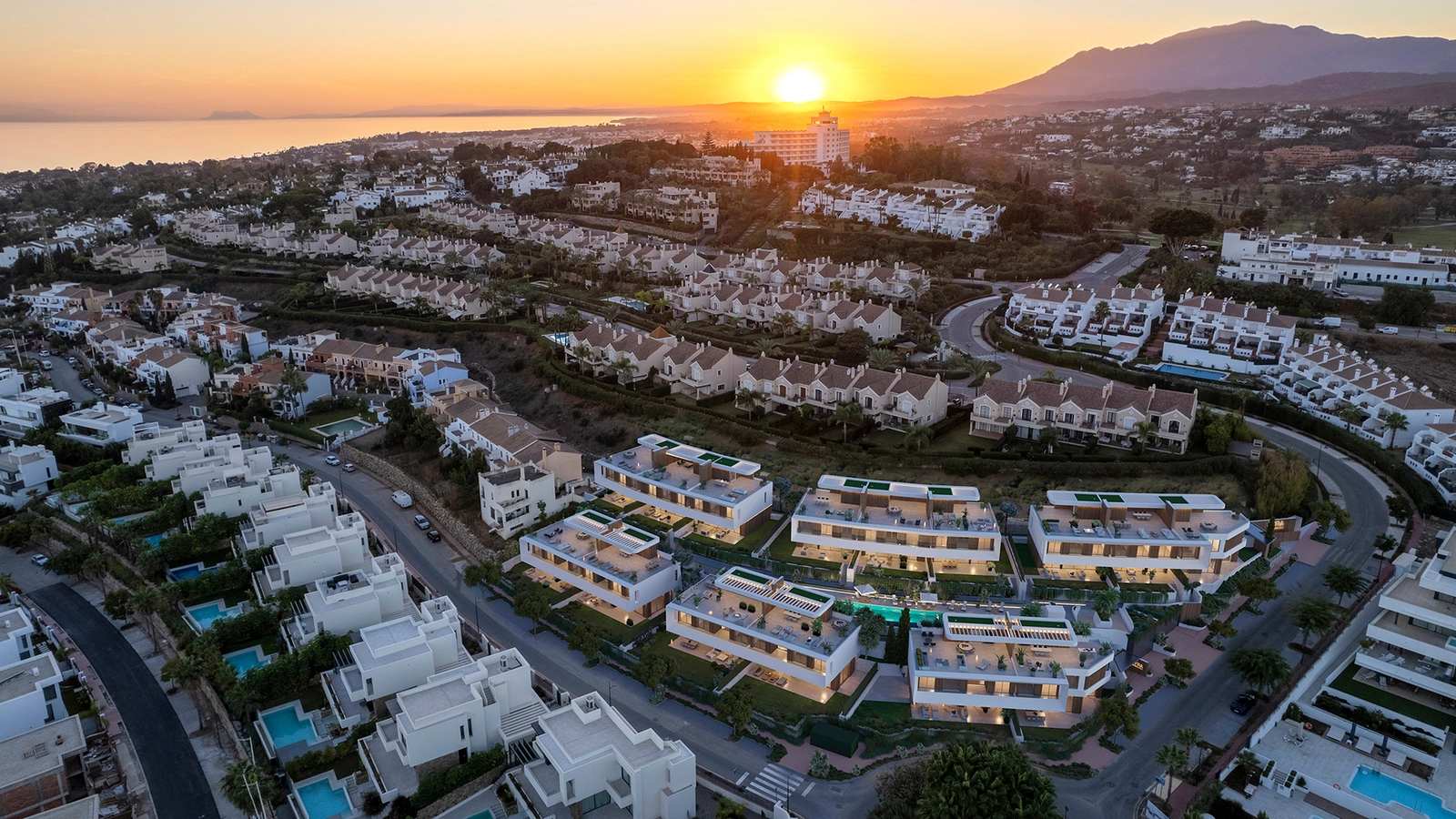 An aerial view of the development at sunset, showing its privileged location near the sea and mountains.
