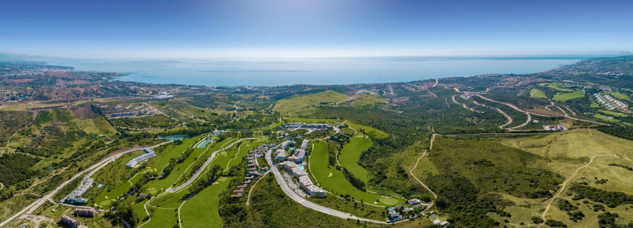 An expansive aerial view of the Sunny Golf development, perfectly integrated with the lush green fairways of Estepona Golf and the sparkling Mediterranean Sea beyond.